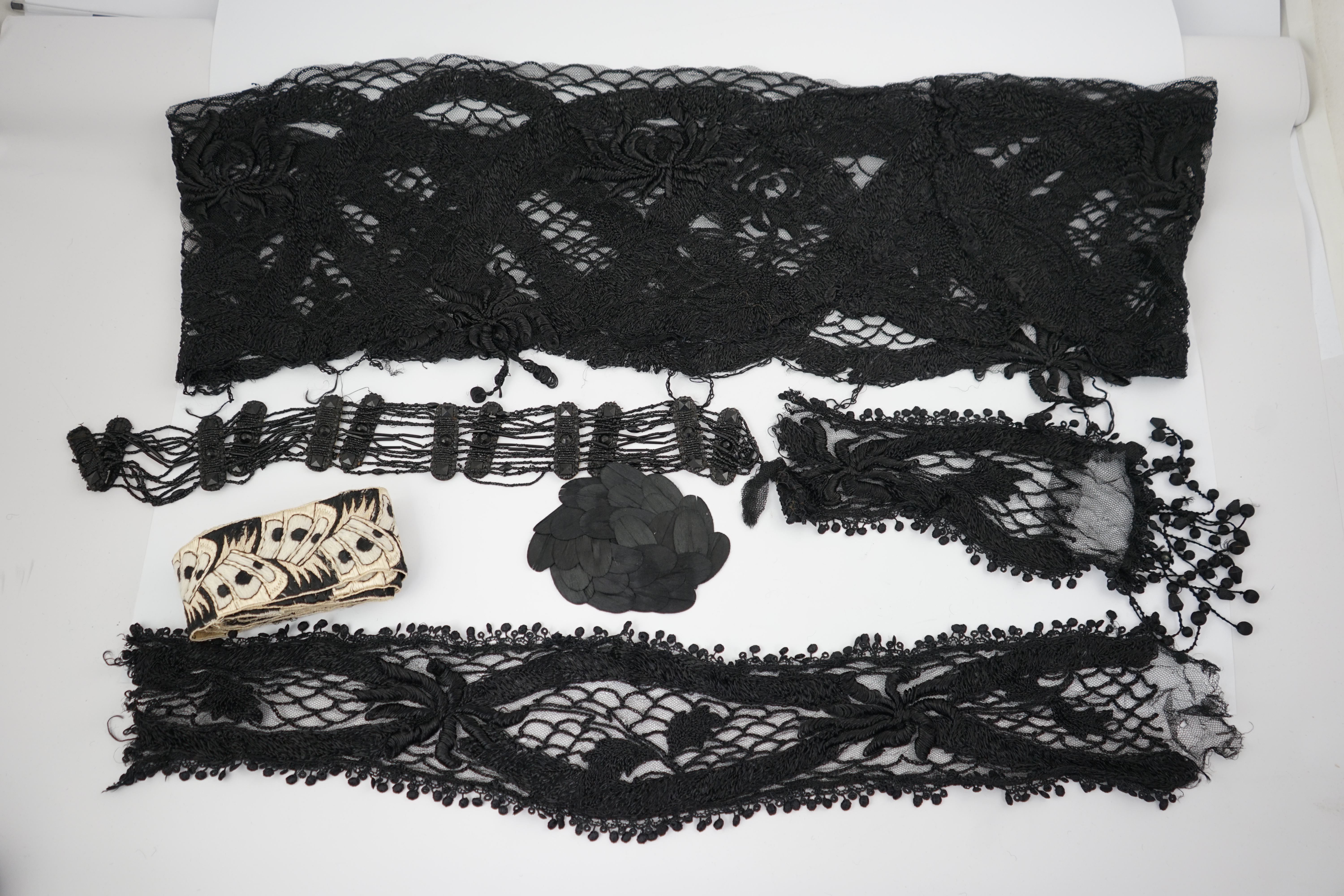 An 1930's black sequin cape, trimmings and lace, an Art Deco black sequin decorated cape on black net, an Edwardian jet beaded belt, a Spanish silk fall cap, three panels of black machine lace, a long length black and cr